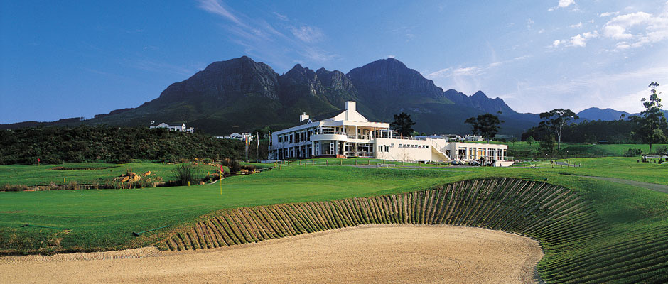 A large white house is sitting on top of a golf course with mountains in the background.