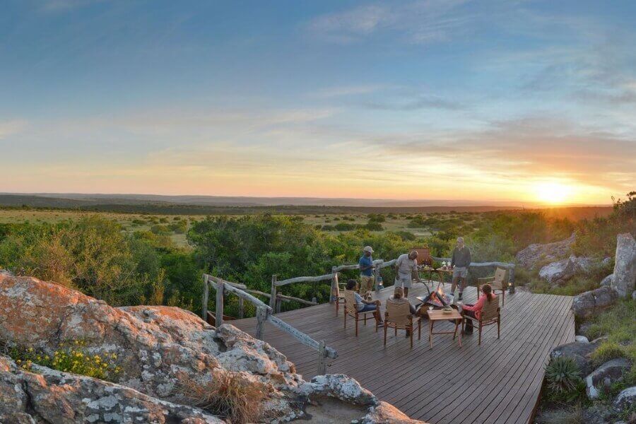 A group of people are sitting on a wooden deck overlooking a sunset.
