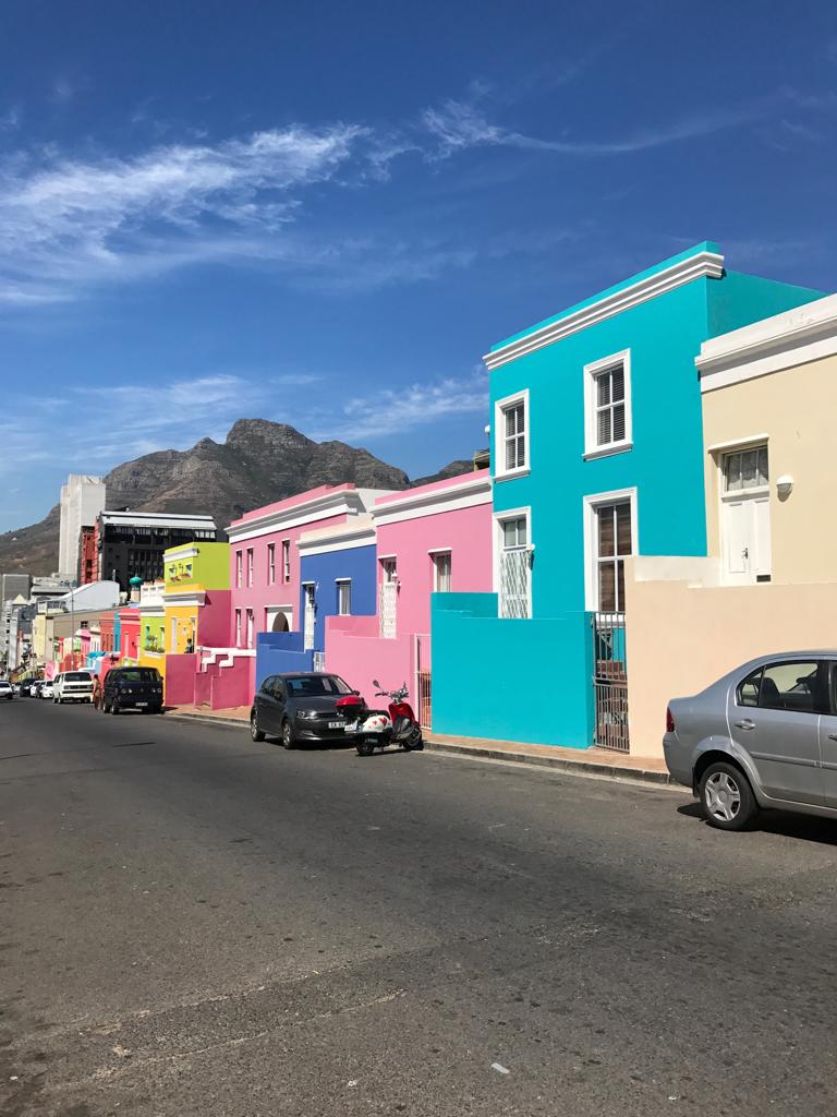 A row of colorful houses with cars parked on the side of the road.