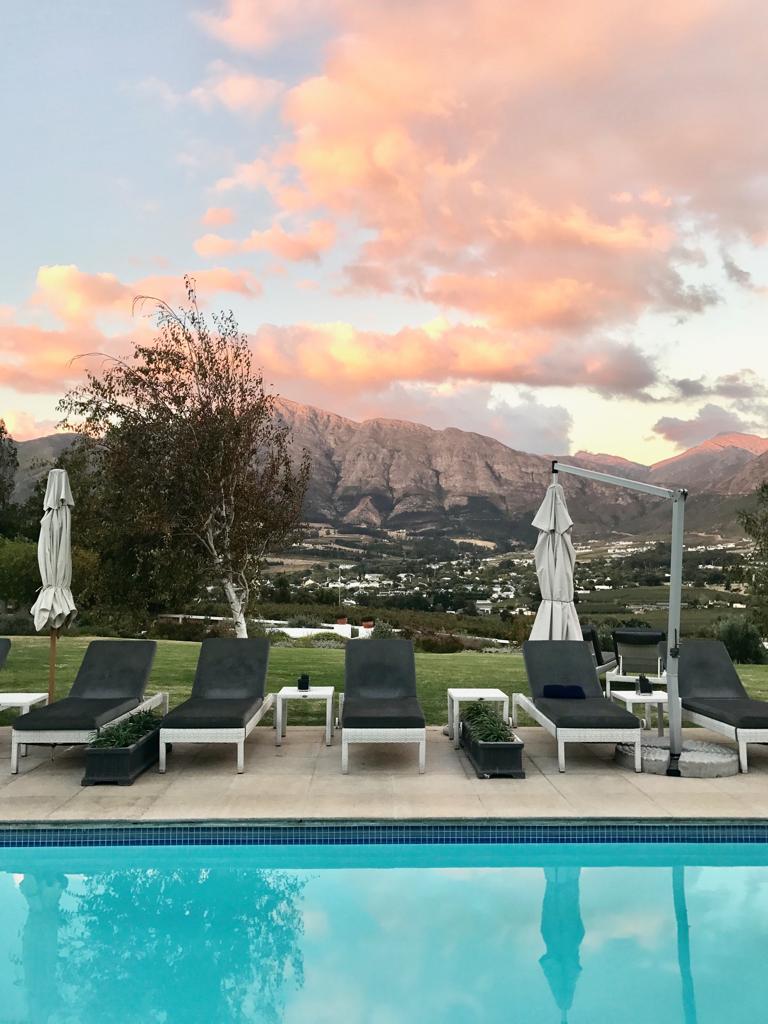 A swimming pool surrounded by chairs and umbrellas with mountains in the background.