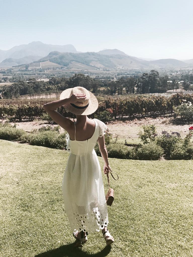 A woman in a white dress and straw hat is standing in a grassy field.