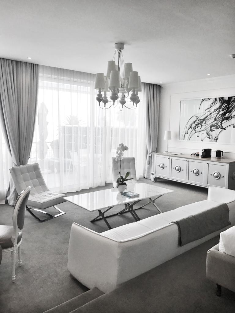 A black and white photo of a living room with a couch , chairs , coffee table and chandelier.