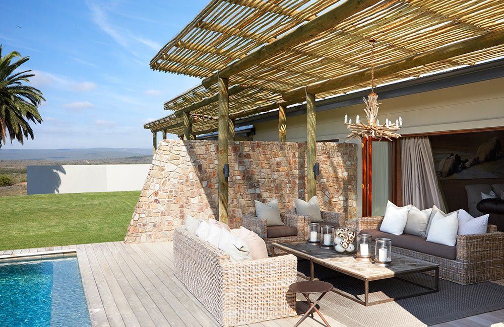 There is a swimming pool in the background and a patio with furniture and a pergola.