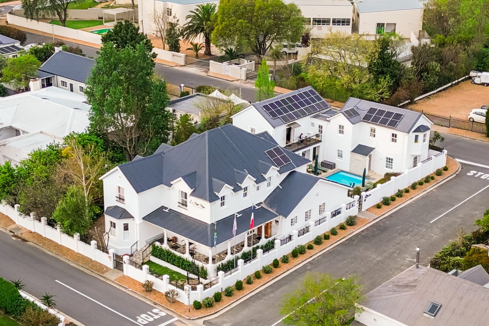 An aerial view of a large white house with a swimming pool surrounded by trees.