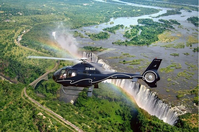 A helicopter is flying over a waterfall with a rainbow in the background