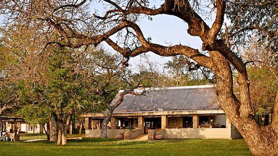 A house in the middle of a lush green field surrounded by trees.