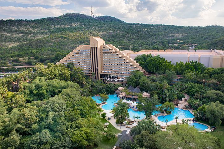 An aerial view of a large hotel surrounded by trees and swimming pools.