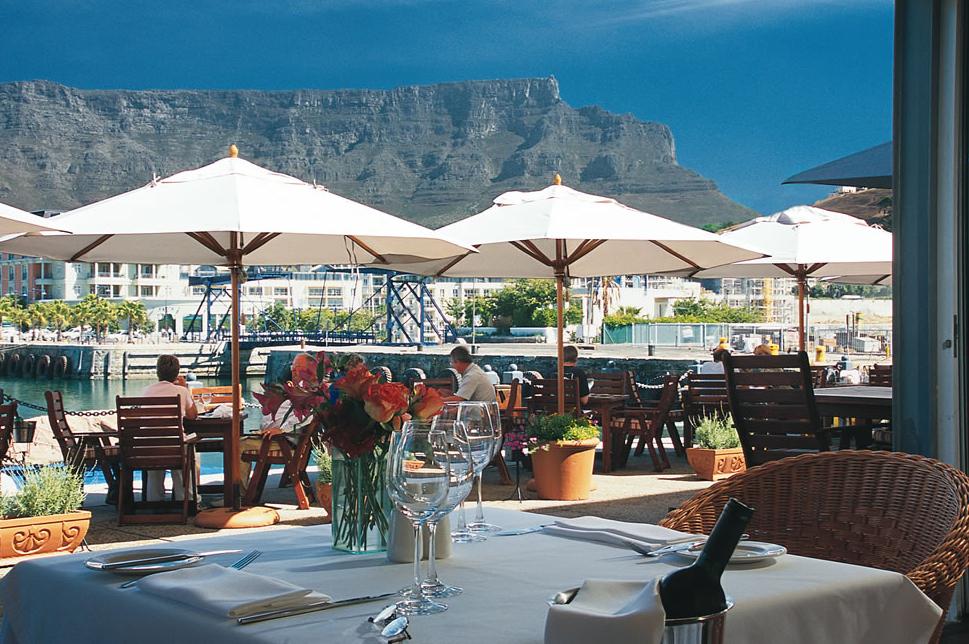 A restaurant with tables and chairs and umbrellas with a mountain in the background