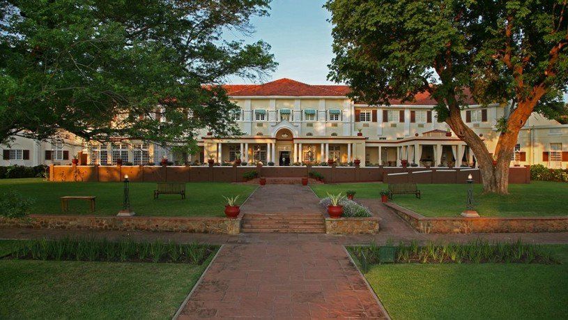 A large white building with a red roof is surrounded by trees and grass.
