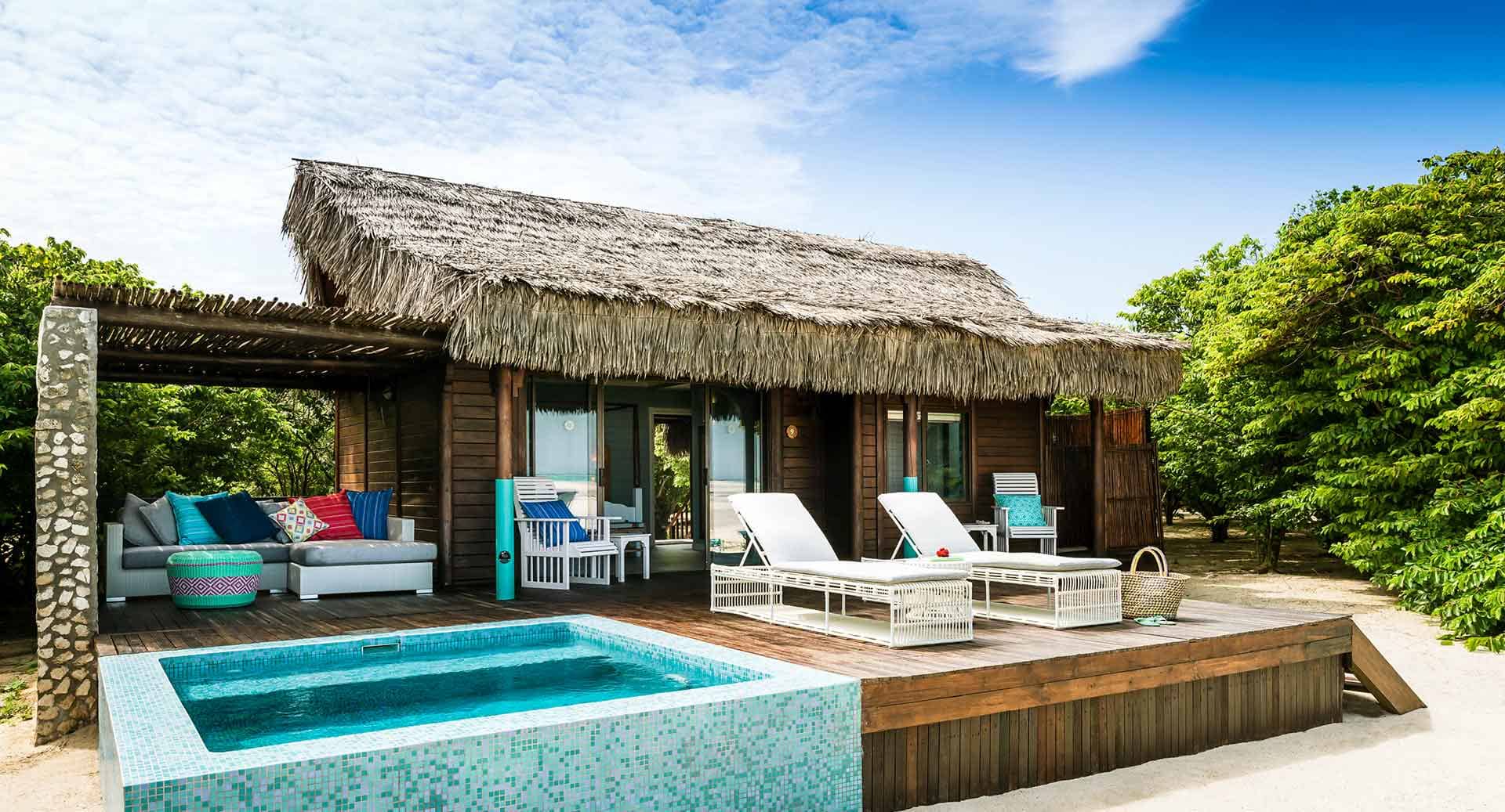 A small house with a thatched roof and a pool in front of it.