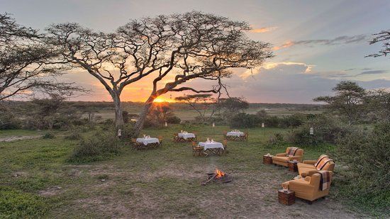 A sunset over a field with tables and chairs and a fire pit.