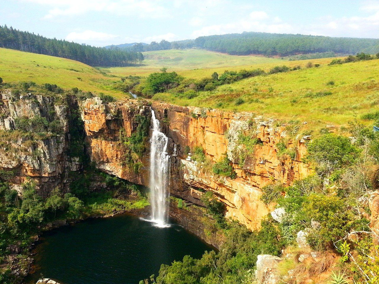 A waterfall is surrounded by trees and grass in the middle of a valley.