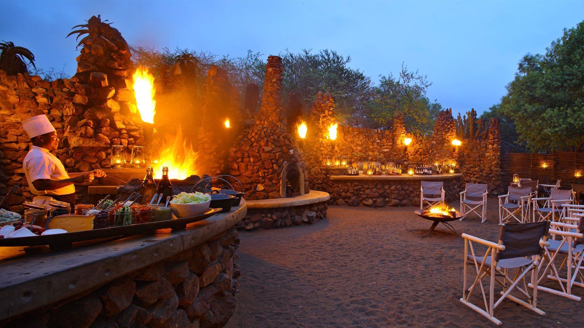 A man is cooking food in front of a fire pit.