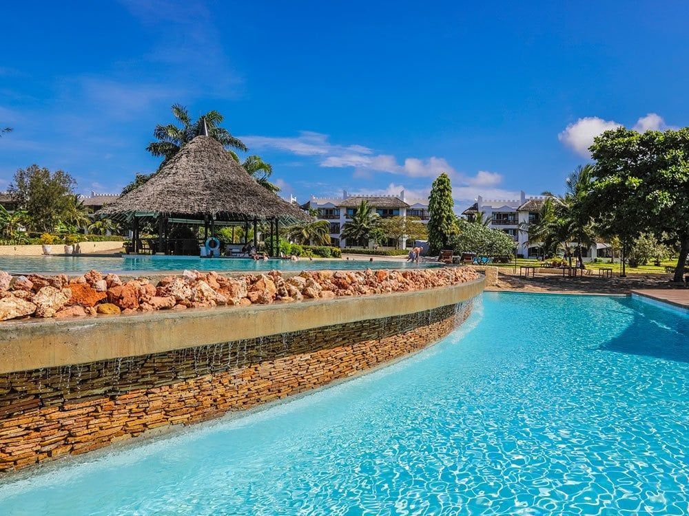 A large swimming pool with a thatched hut in the background.
