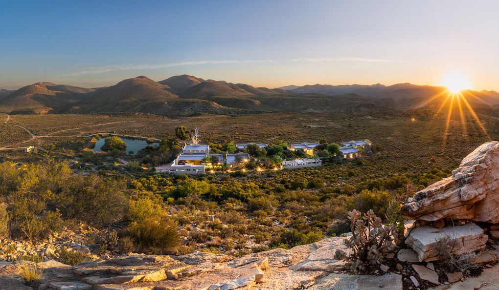 The sun is setting over a desert landscape with mountains in the background.
