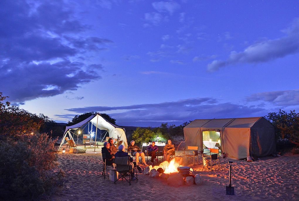 A group of people are sitting around a campfire in front of a tent.