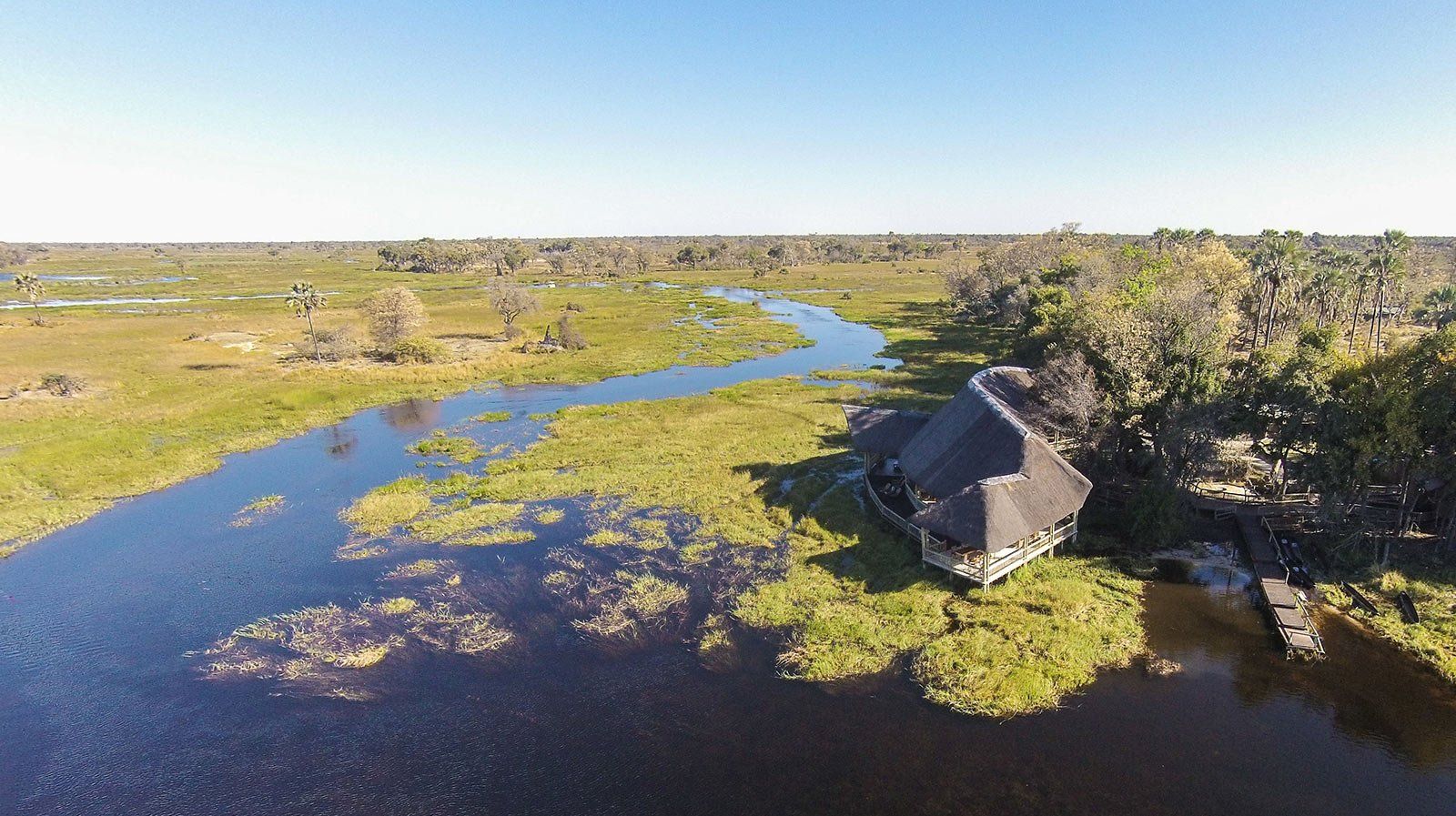 An aerial view of a house in the middle of a swamp next to a river.