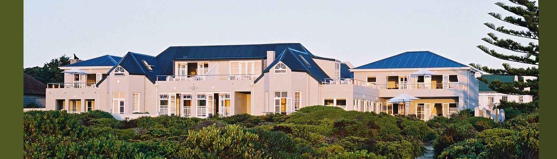 A large white house with blue roofs is surrounded by trees