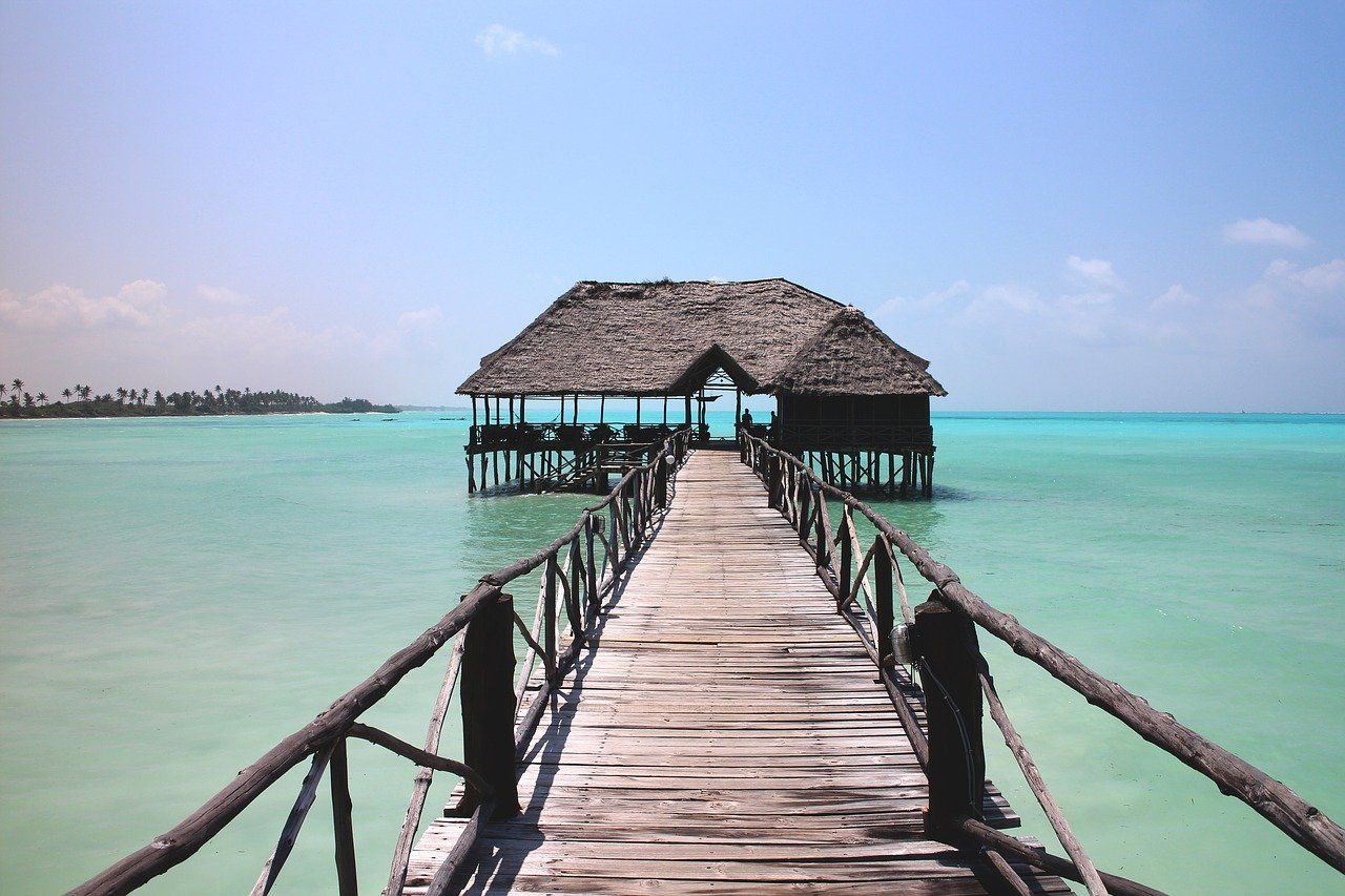 A wooden pier leading to a small hut in the middle of the ocean.
