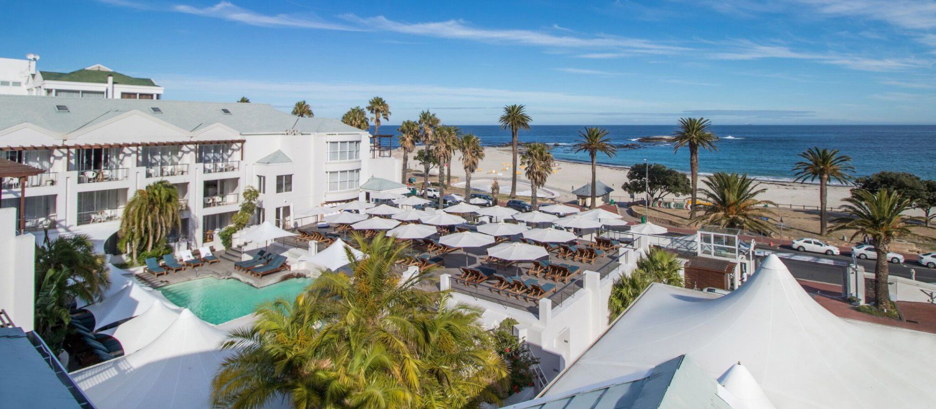 An aerial view of a hotel with a pool and a beach in the background.