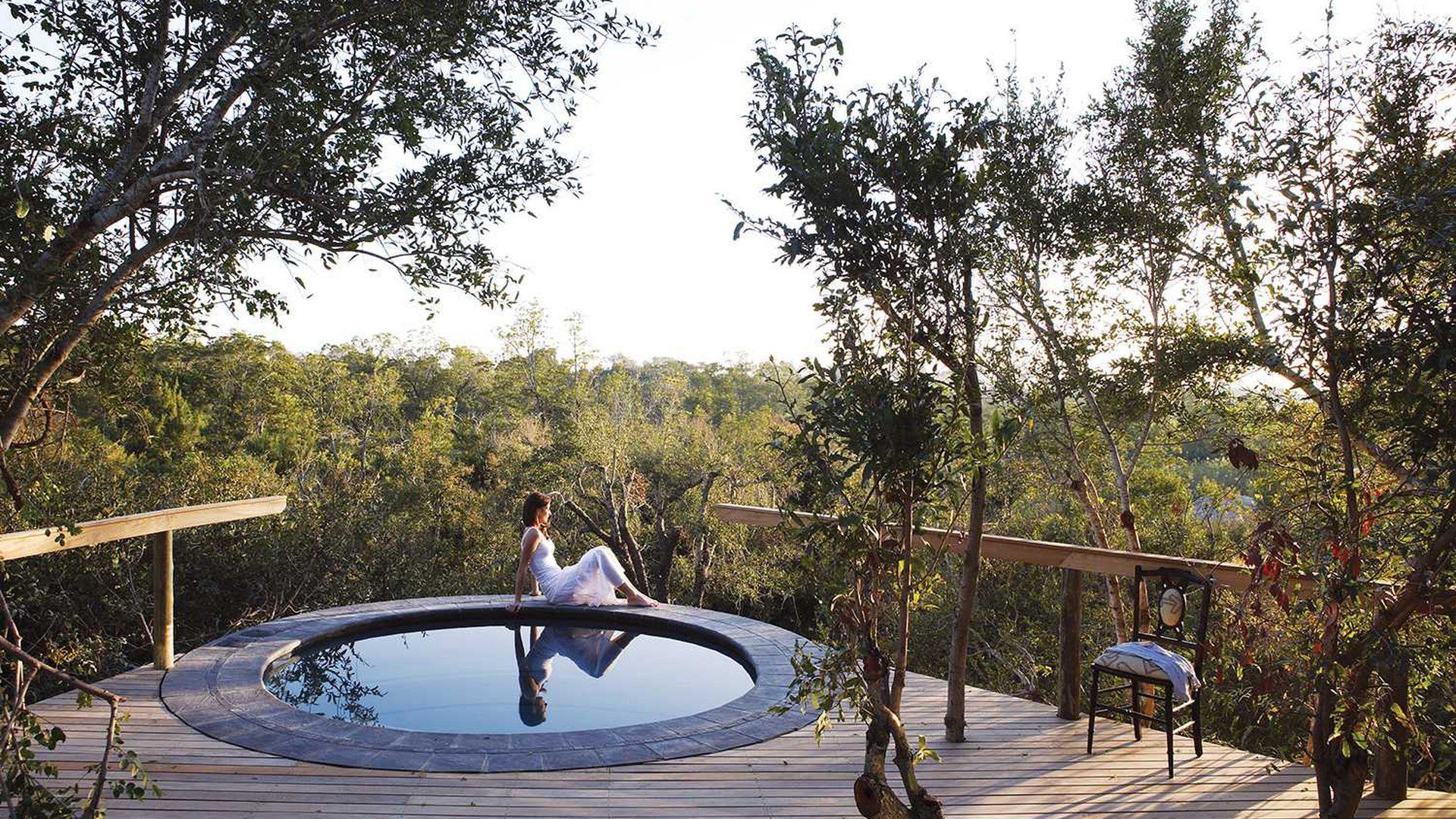 A woman sits on the edge of a pool surrounded by trees
