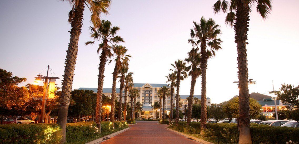 A row of palm trees along a road leading to a large building