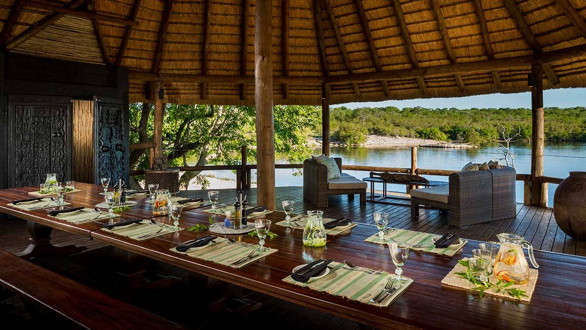 A long wooden table with a thatched roof overlooking a lake.