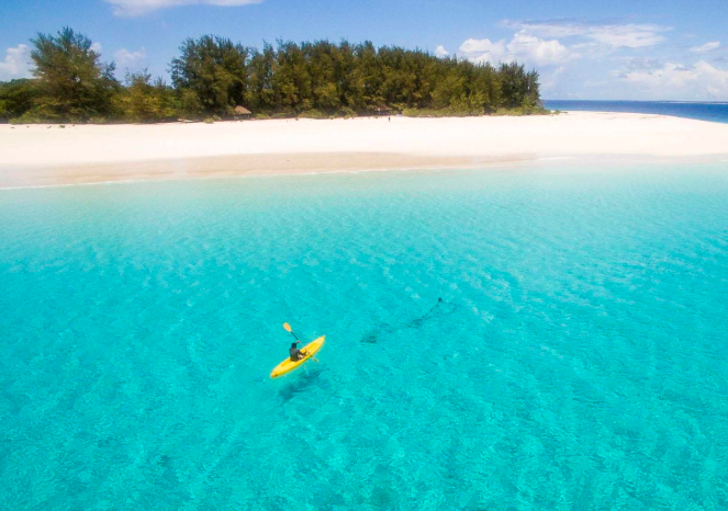 A person is kayaking in the ocean near a small island.