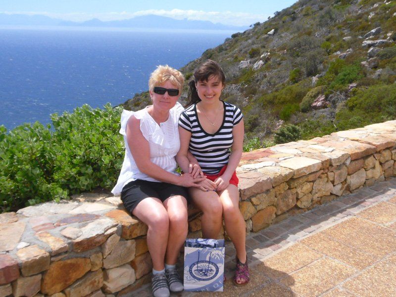 Two women sit on a stone wall overlooking the ocean