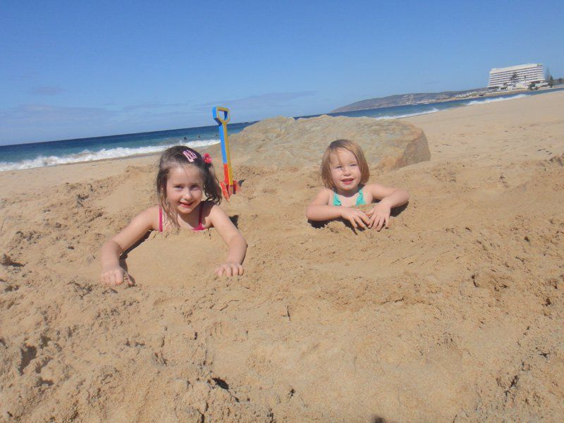 Two little girls are buried in the sand on a beach
