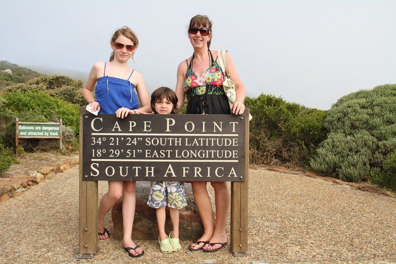 Three people standing in front of a sign that says cape point south africa