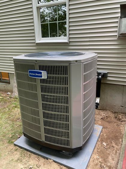 A large air conditioner is sitting outside of a house next to a window.