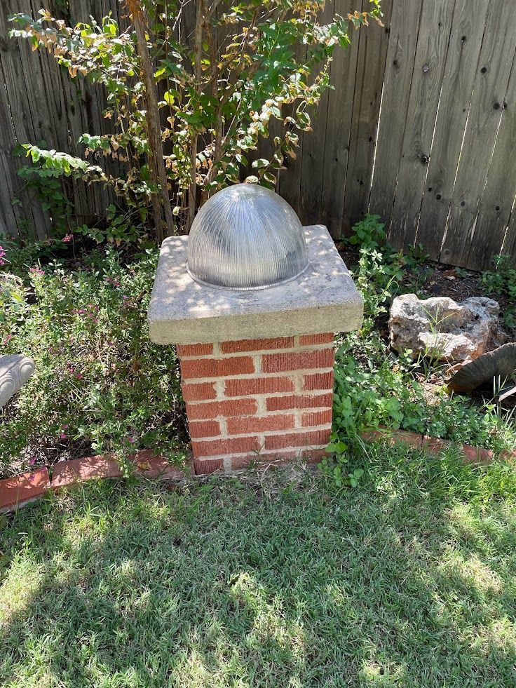 A brick chimney with a ball on top of it in a yard.