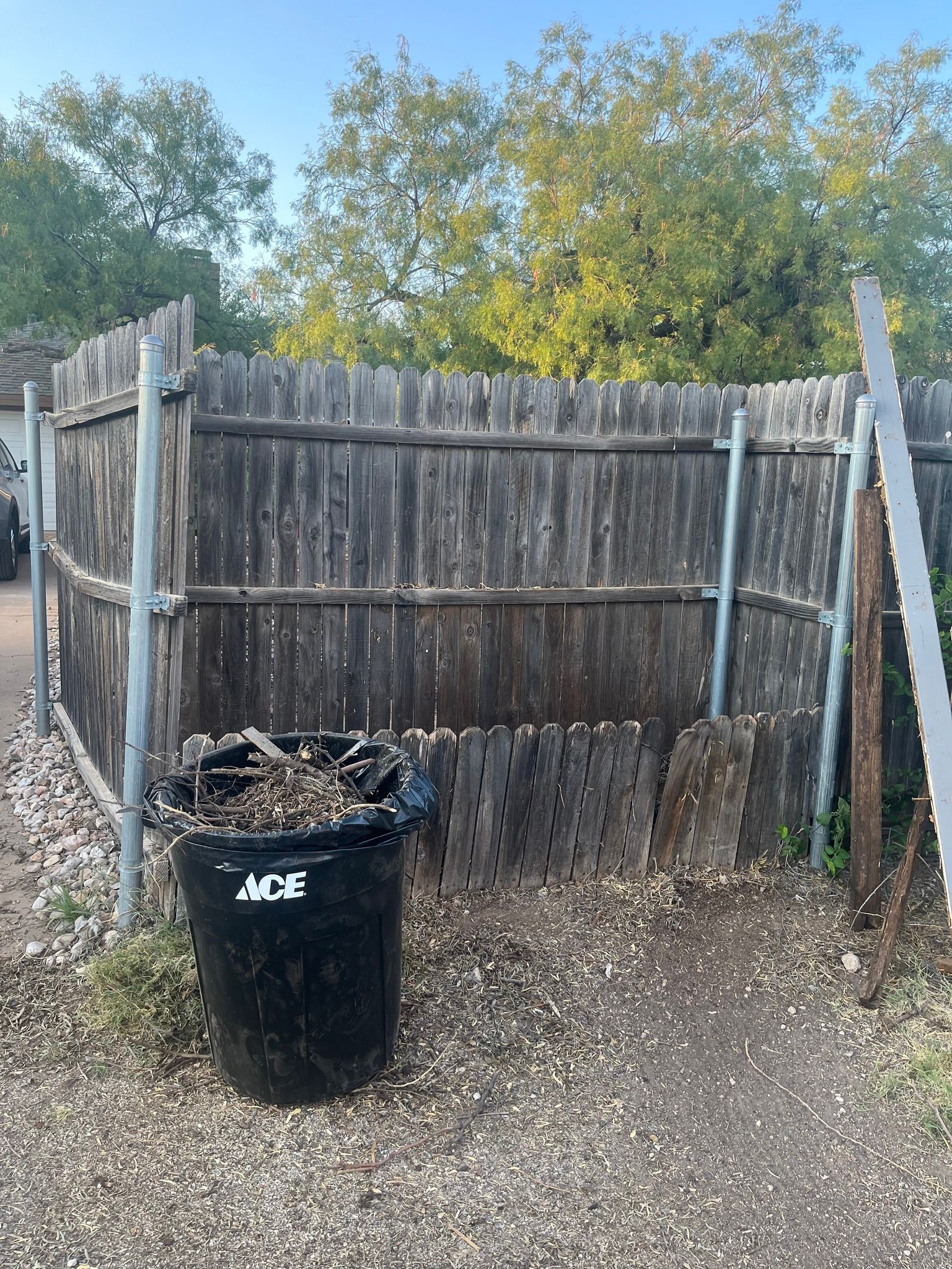 A black trash can is sitting in front of a wooden fence.