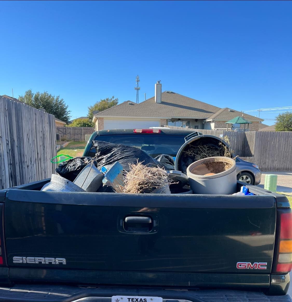 The back of a black sierra truck is filled with trash.