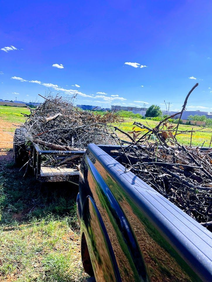A truck is pulling a trailer full of branches in a field.