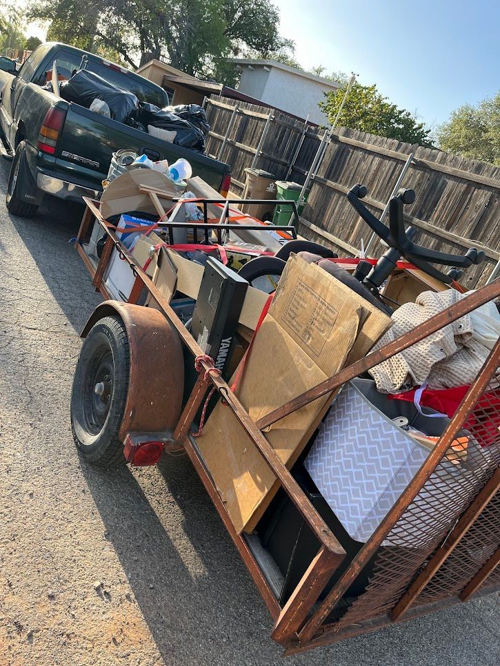 A trailer filled with lots of junk is parked next to a truck.