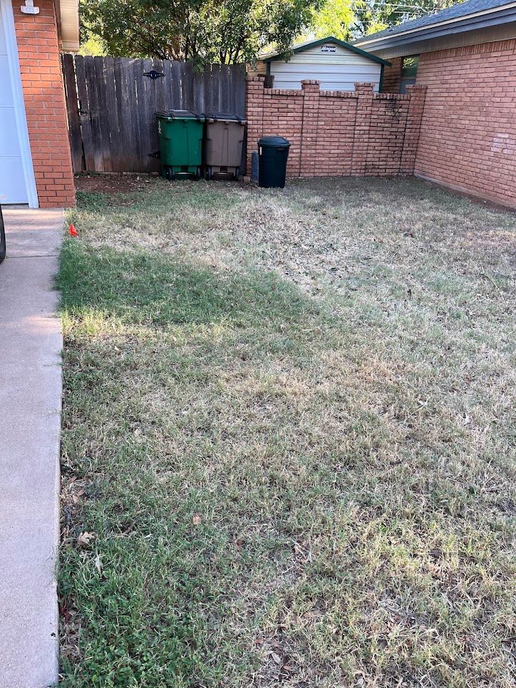 A backyard with a fence and trash cans in it.