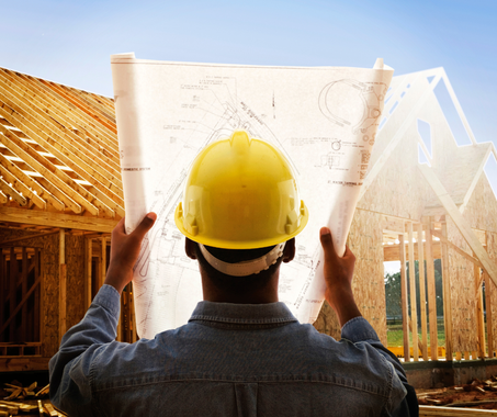A man wearing a hard hat is looking at a blueprint of a house under construction
