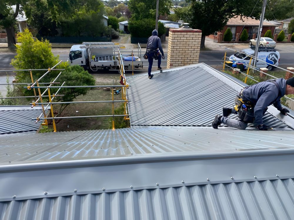 Two Construction Workers Are Working on the Roof of a Building — iFix Roofing Bendigo in Bendigo, VIC