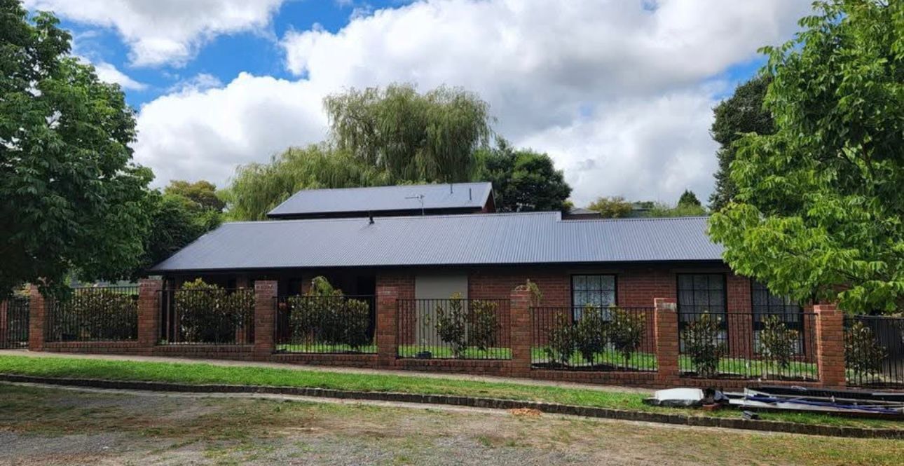 A Large Brick House With a Black Roof and a Fence Surrounding It — iFix Roofing Bendigo in Castlemaine, VIC