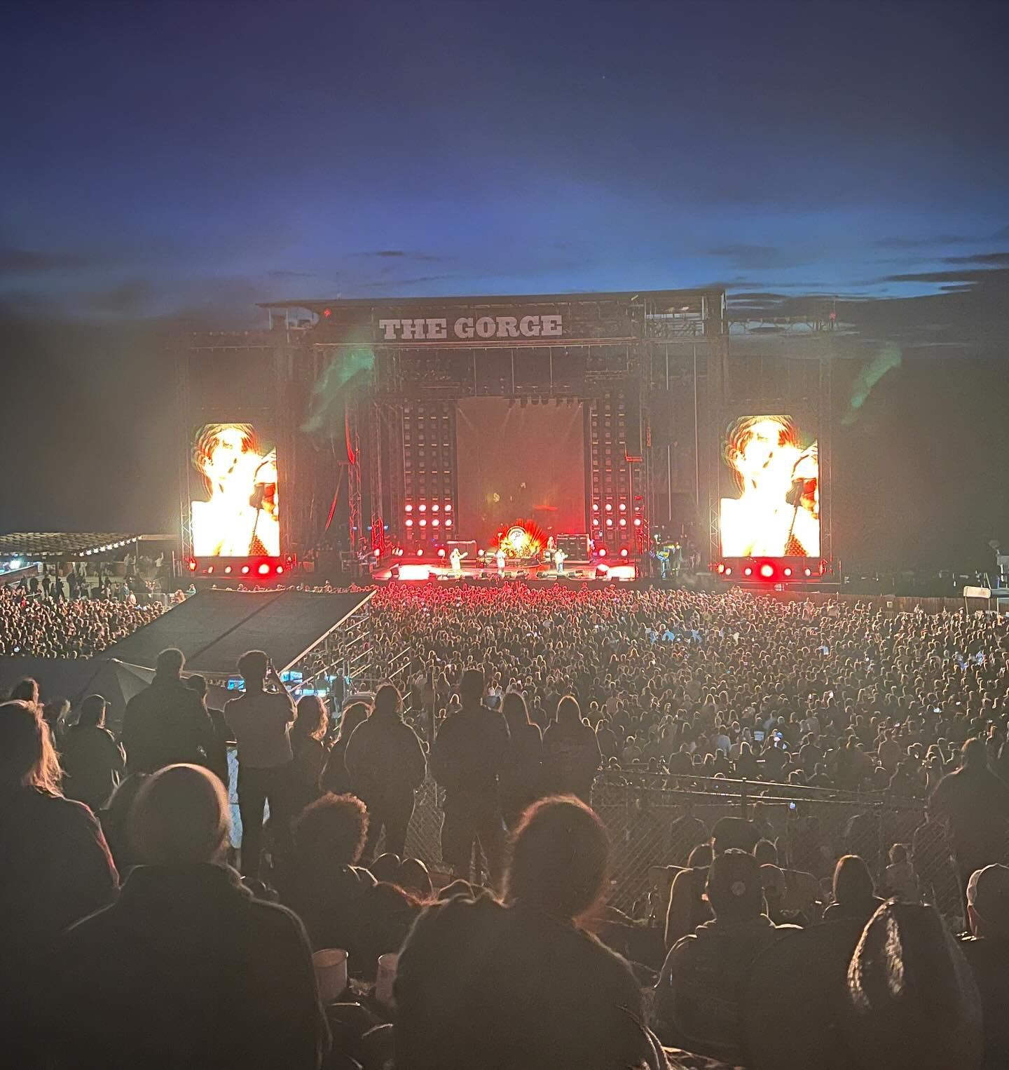 Large outdoor concert with stage lights illuminating the band and a large crowd.