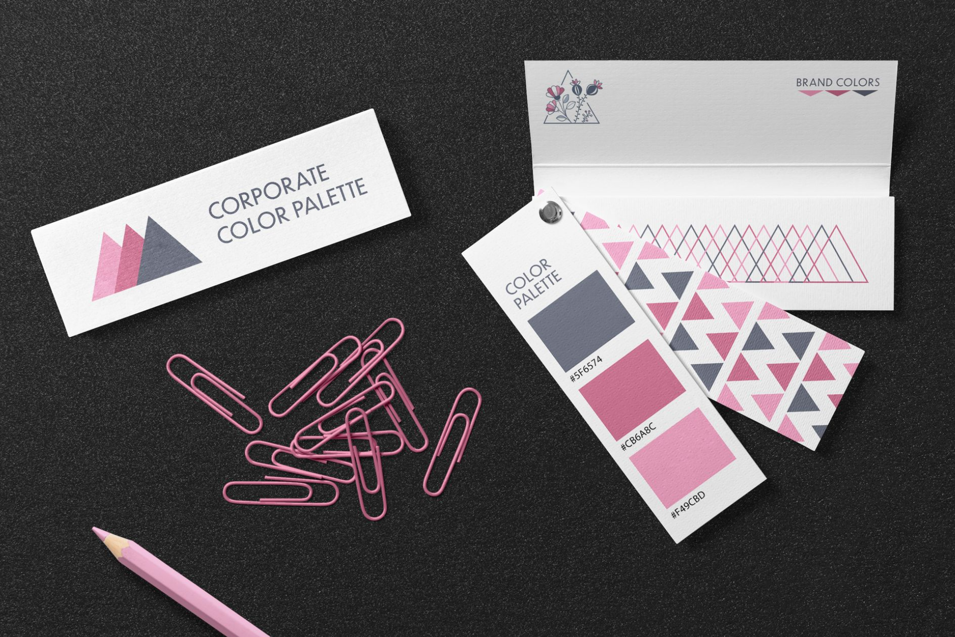 Corporate color palette with pink and gray accents, paperclips, and pencil on a black surface.