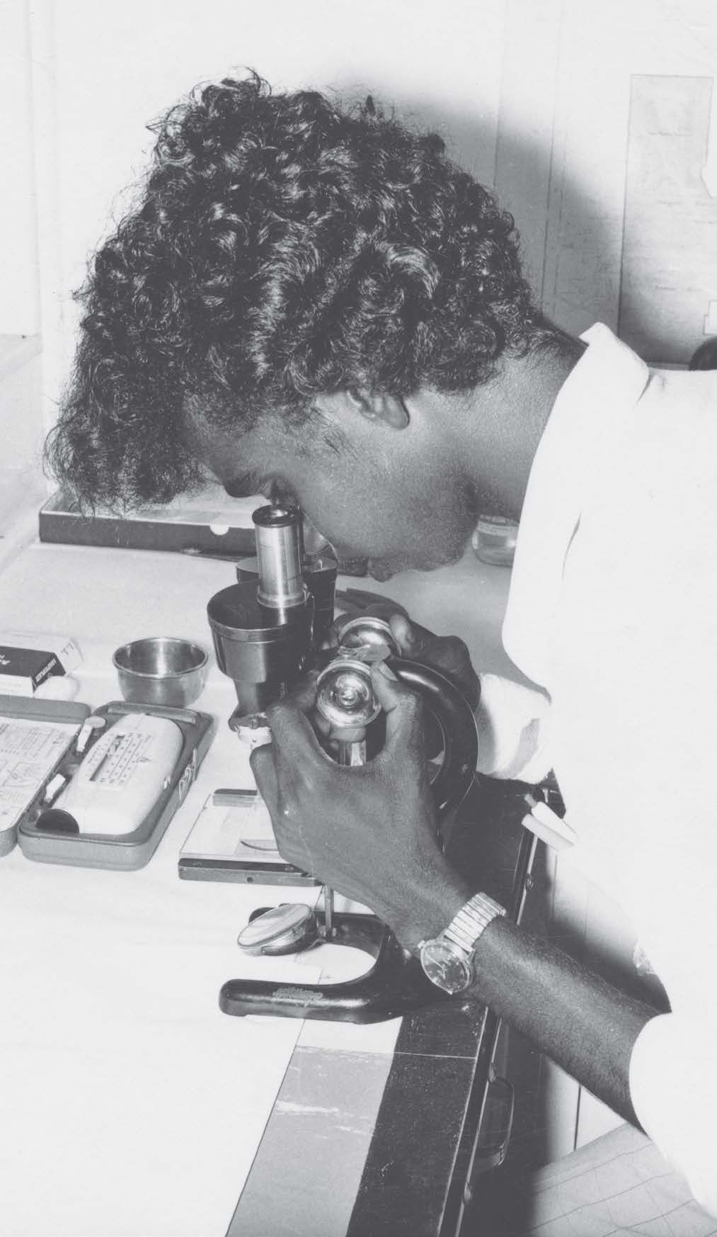 Person with curly hair looking into a microscope in a lab setting.