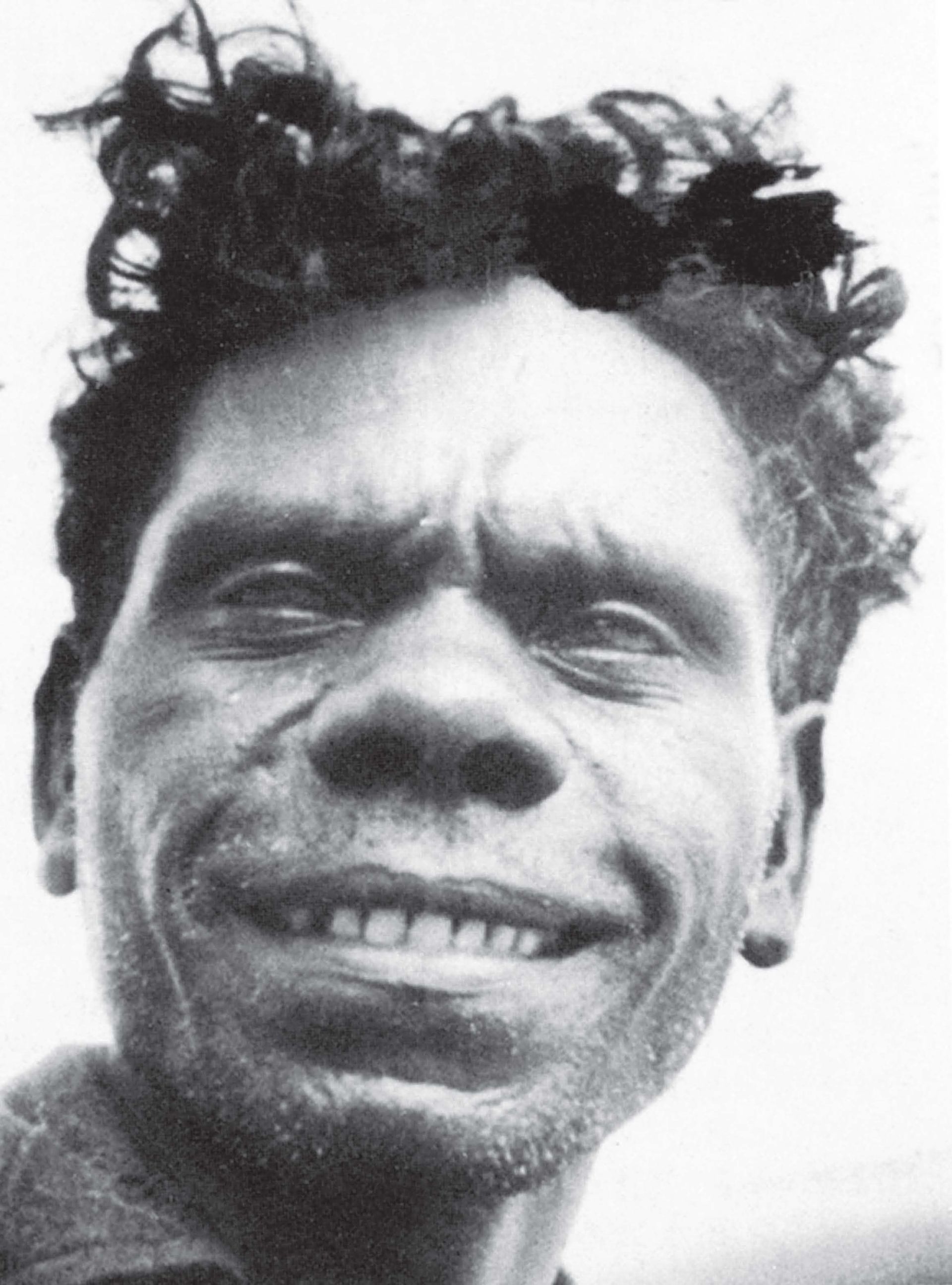 Close-up black and white portrait of an Indigenous man smiling, looking directly at the camera.