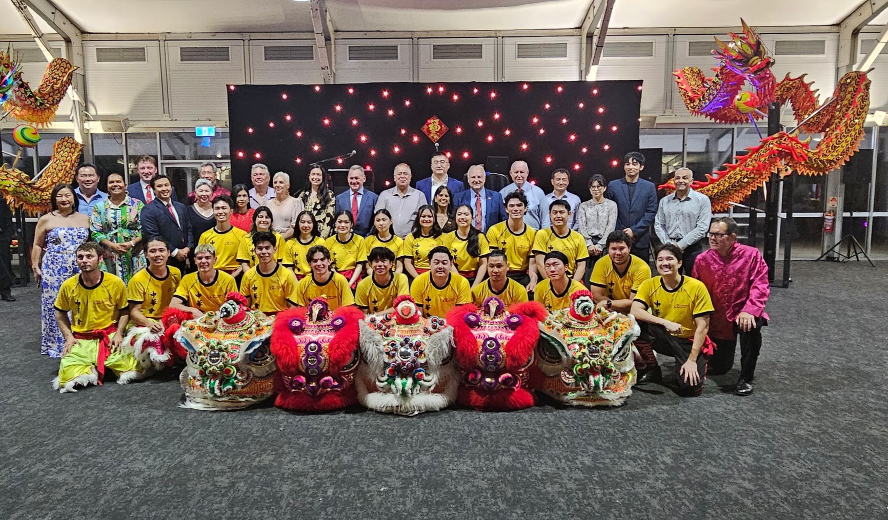 Group poses with red lion dance costumes and banners in an outdoor setting.