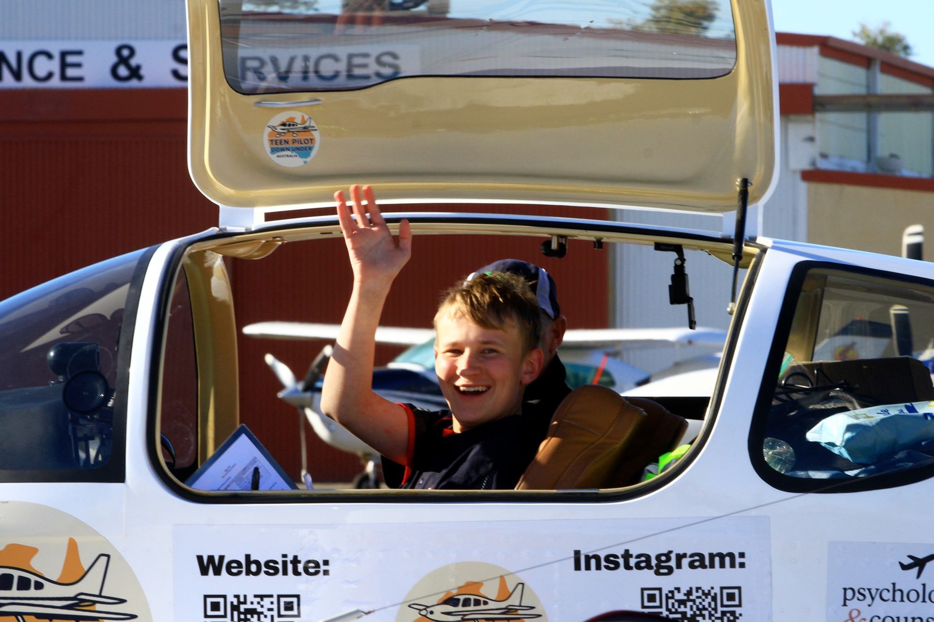 Boy waving from a plane cockpit with a sunny smile, at an airport.