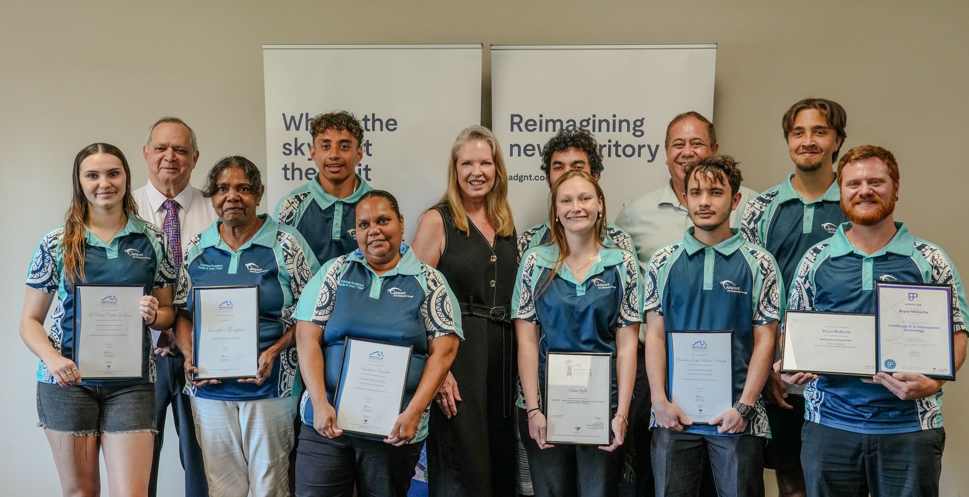 Group of people holding certificates, smiling in front of a banner.