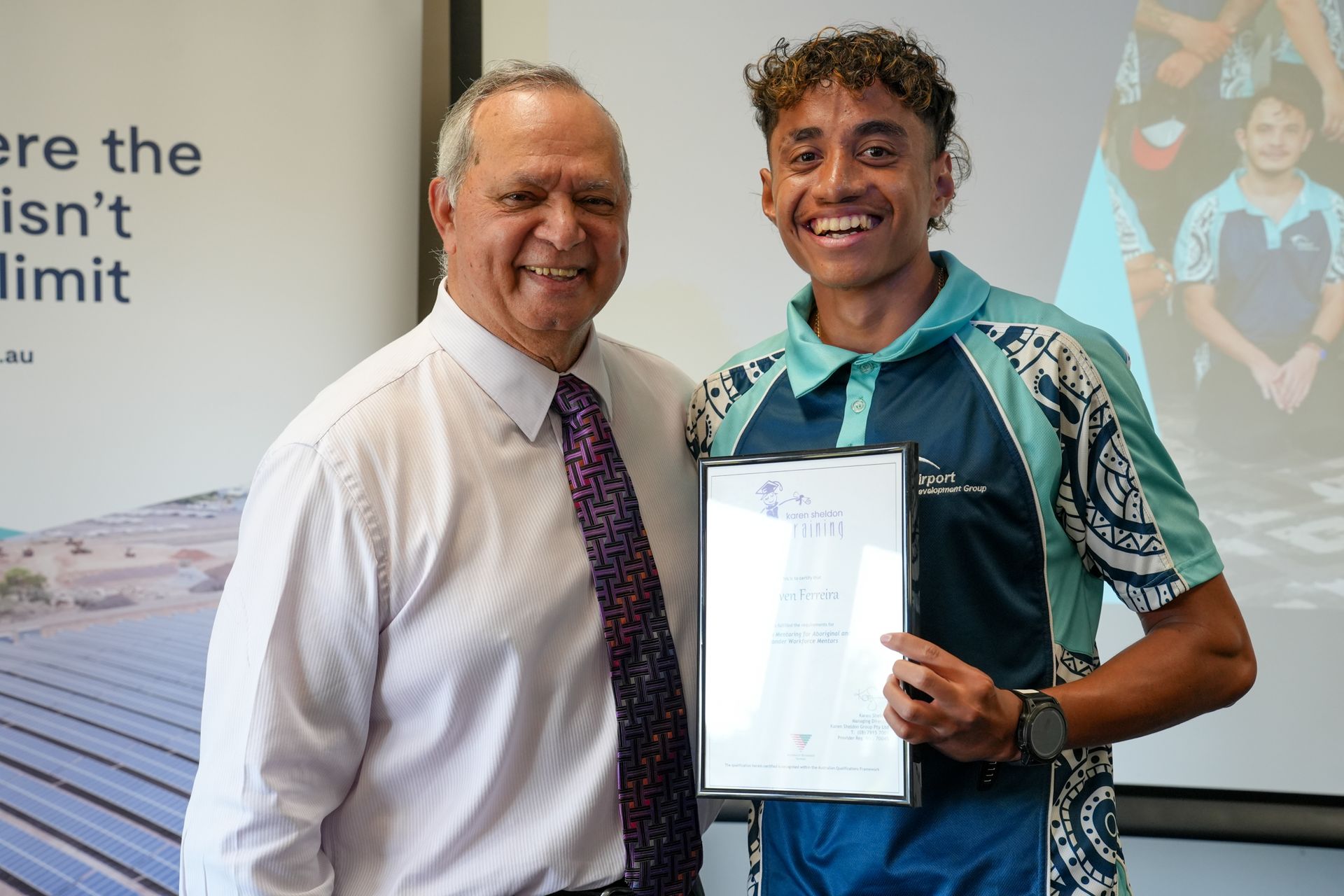 Man presents certificate to smiling young man in front of a backdrop with text and a solar panel illustration.