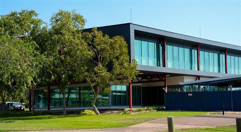 Modern building with glass windows and dark trim, trees in front, blue sky.
